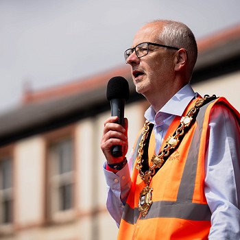 dyn mewn gwisg oren hi-vis yn siarad i mewn i feicroffon