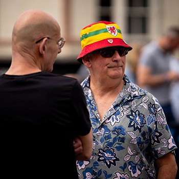 2 ddyn yn siarad, un yn gwisgo het Cymru